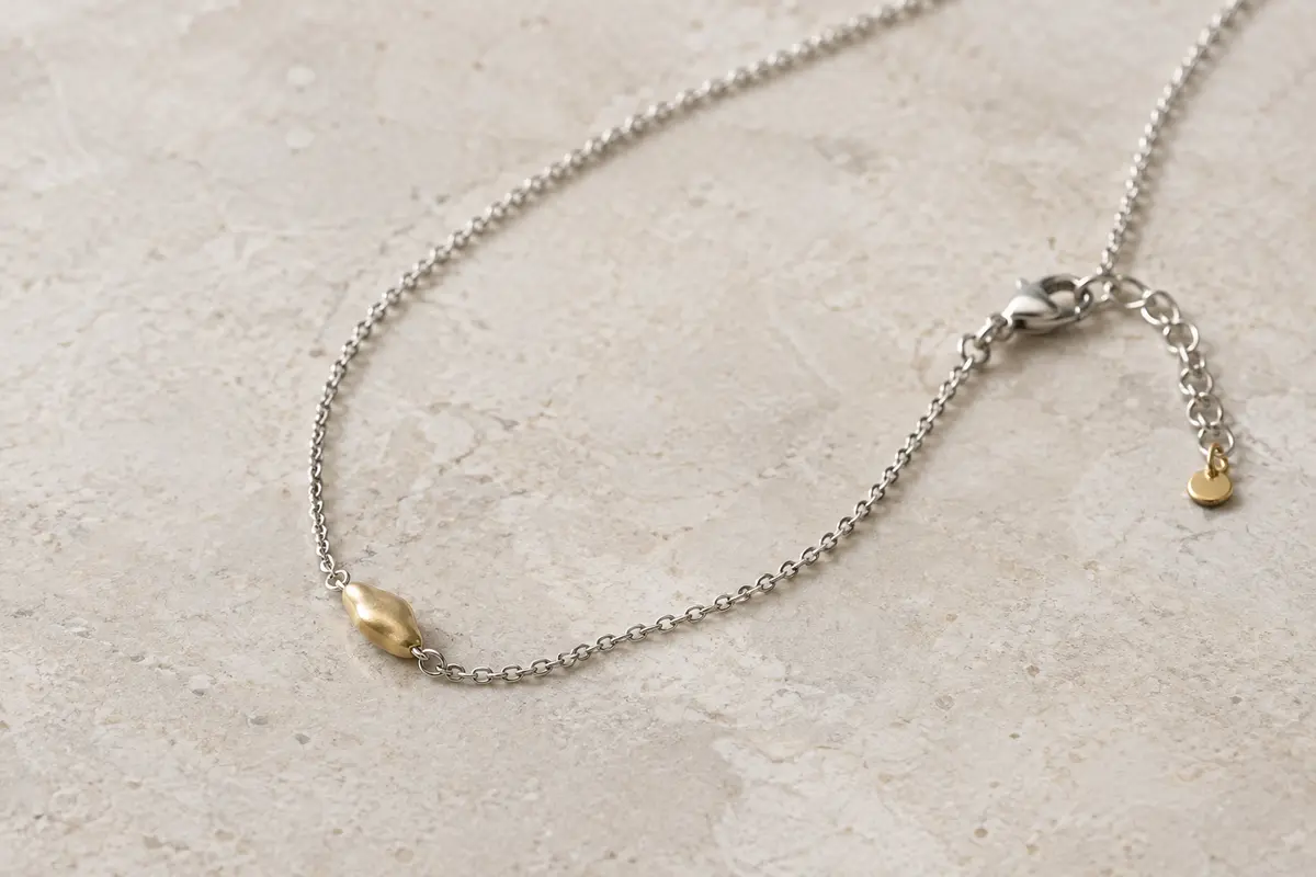 Gros plan d’un collier argenté et doré montrant la chaîne, le pendentif et le fermoir