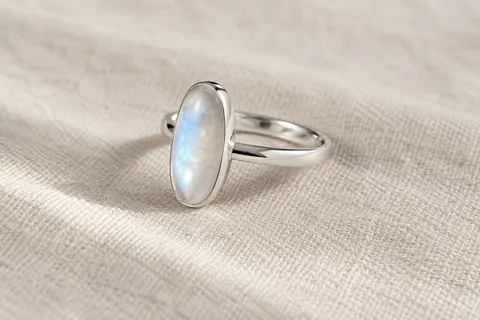 Bague en argent 925 plaqué or blanc avec une pierre de lune centrale, posée sur du lin ivoire.