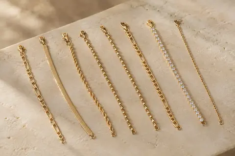 Sept bracelets chaîne Adramata aux styles variés, disposés sur une surface minérale claire