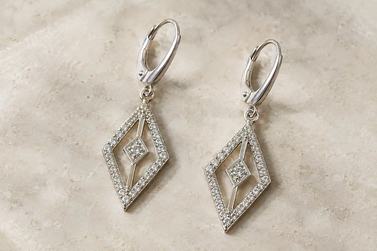 Boucles d’oreilles pendantes ajourées ornées de zircones, présentées seules sur une surface minérale claire.