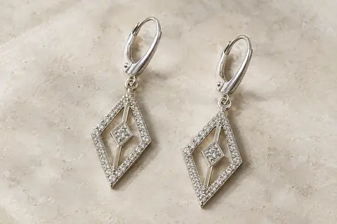 Boucles d’oreilles pendantes ajourées ornées de zircones, présentées seules sur une surface minérale claire.