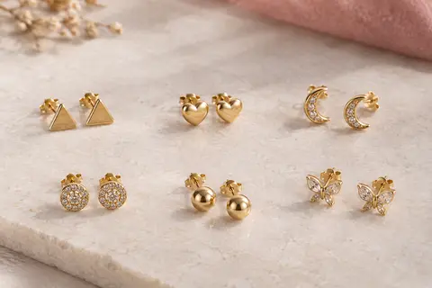 Six paires de puces d’oreilles de ton doré aux motifs variés présentées sur une surface claire