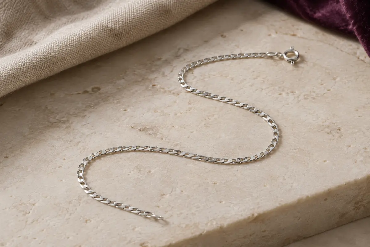 Chaîne gourmette fine en argent sterling disposée en courbe sur une surface minérale claire