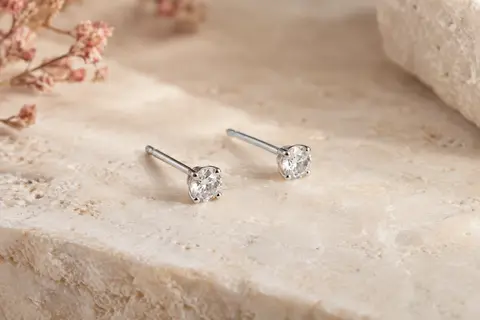 Paire de petites puces Amberta en argent 925 avec zircones cubiques, posées sur une surface claire.