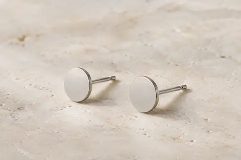 Puces d’oreilles rondes et plates en titane, en finition argentée, posées sur une surface claire.