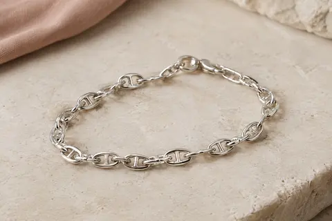 Bracelet chaîne marine en argent posé seul sur une surface minérale claire, avec ses maillons visibles