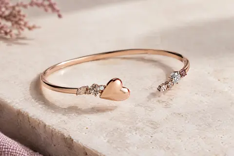 Bracelet-jonc à éléments scintillants et cœur incurvé doré rose posé sur une surface claire.