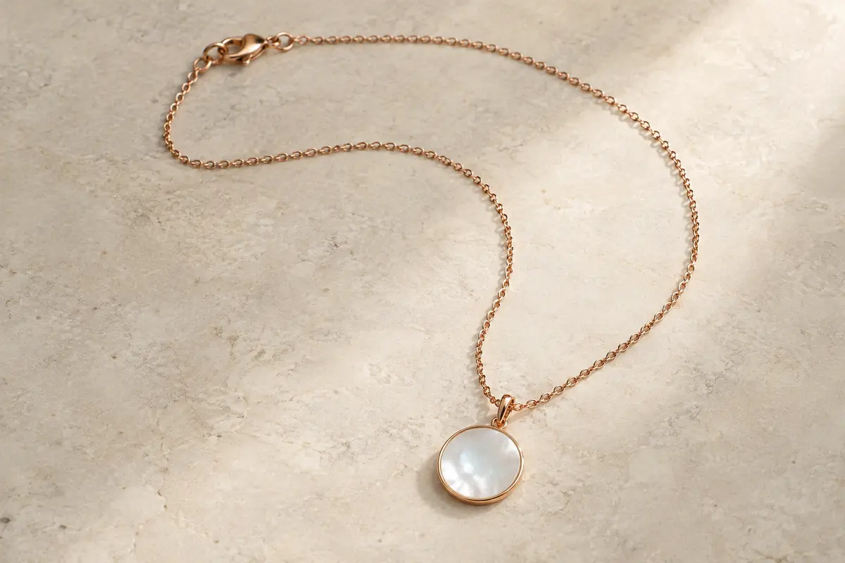 Collier en acier ton or rose avec pendentif rond en nacre posé sur une surface claire