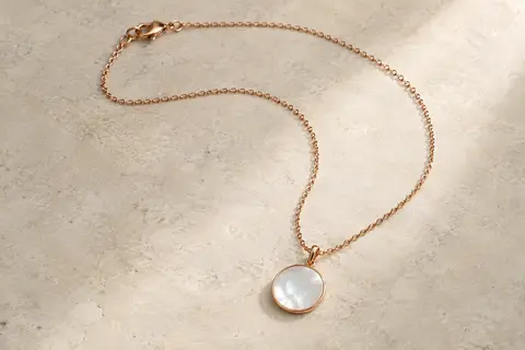 Collier en acier ton or rose avec pendentif rond en nacre posé sur une surface claire