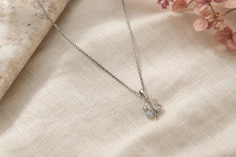Collier sautoir de ton argenté avec chaîne vénitienne et petit pendentif trèfle sur du lin ivoire.