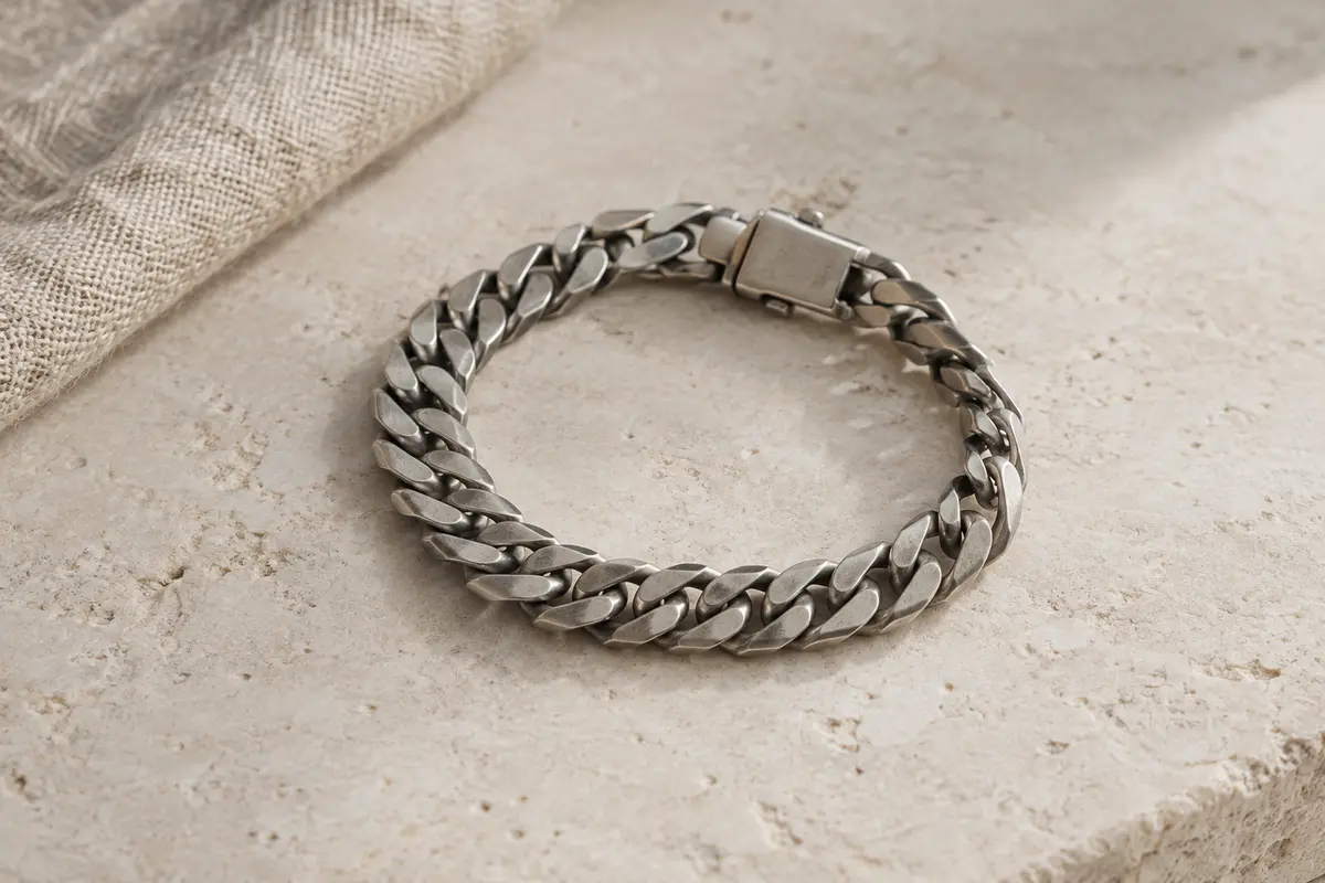 Bracelet chaîne cubaine en acier inoxydable à l’aspect argent antique, posé sur une surface minérale claire.