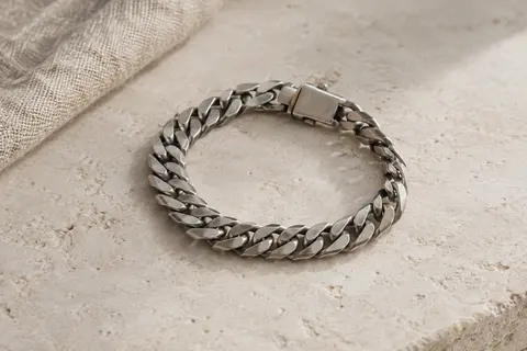 Bracelet chaîne cubaine en acier inoxydable à l’aspect argent antique, posé sur une surface minérale claire.