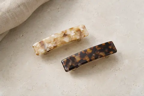 Deux barrettes rectangulaires en acétate à motifs écaille clair et foncé, posées sur une surface claire.