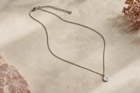 Collier argenté en acier inoxydable avec chaîne ajustable et petite médaille ronde gravée d’une initiale.