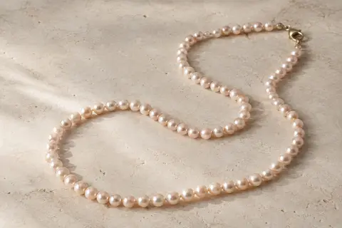 Collier long de perles de 8 mm disposé en courbes sur une surface minérale claire.