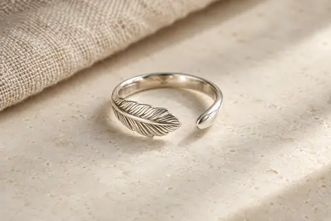 Bague ouverte en argent 925 au motif plume, posée sur une surface minérale claire