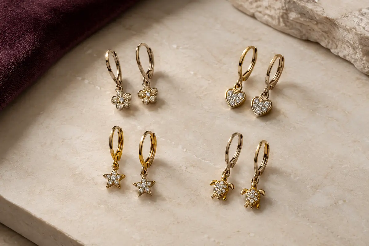 Quatre paires de boucles pendantes JeweBella à motifs fleur, cœur, étoile et tortue, disposées sur une surface claire.