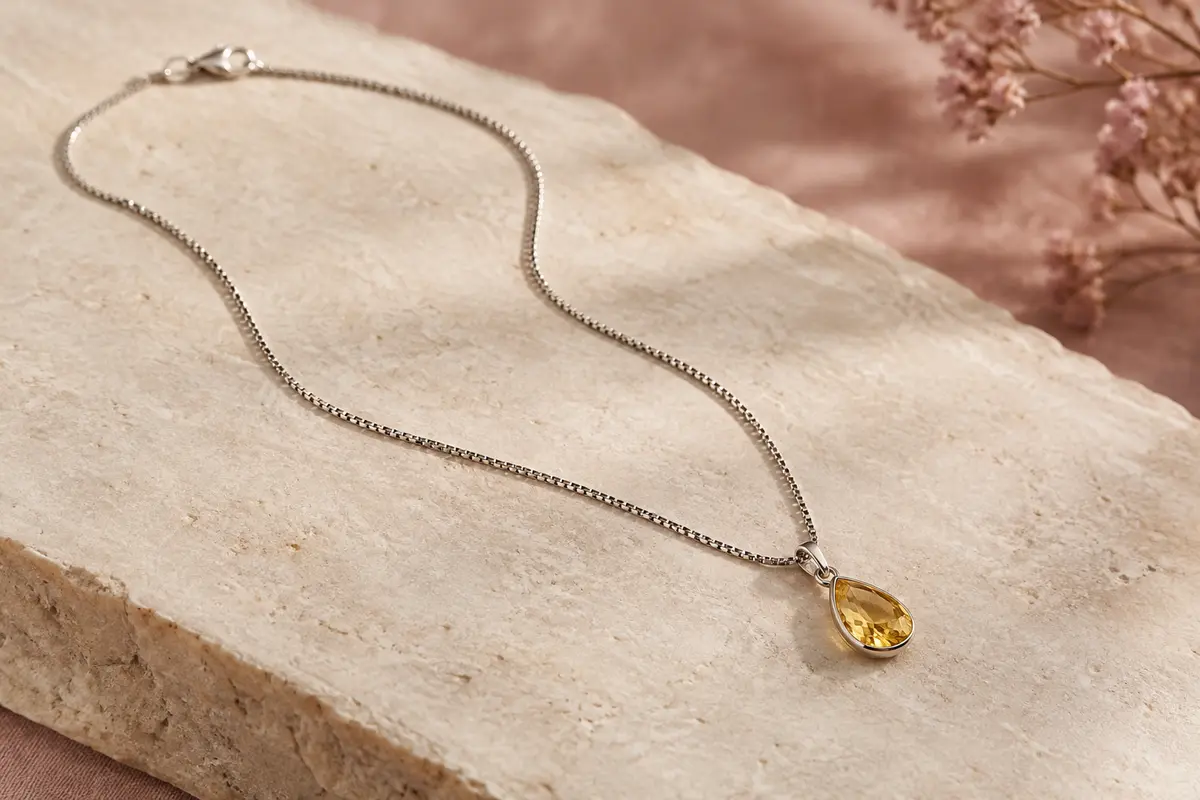 Collier à chaîne vénitienne argentée et petit pendentif en pierre jaune facettée sur fond ivoire