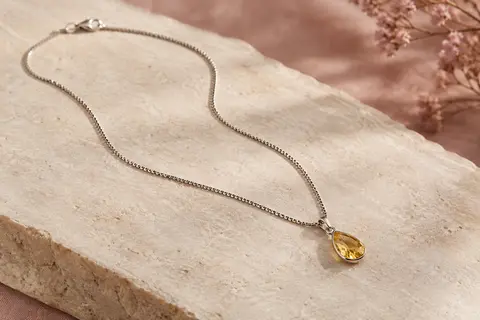 Collier à chaîne vénitienne argentée et petit pendentif en pierre jaune facettée sur fond ivoire