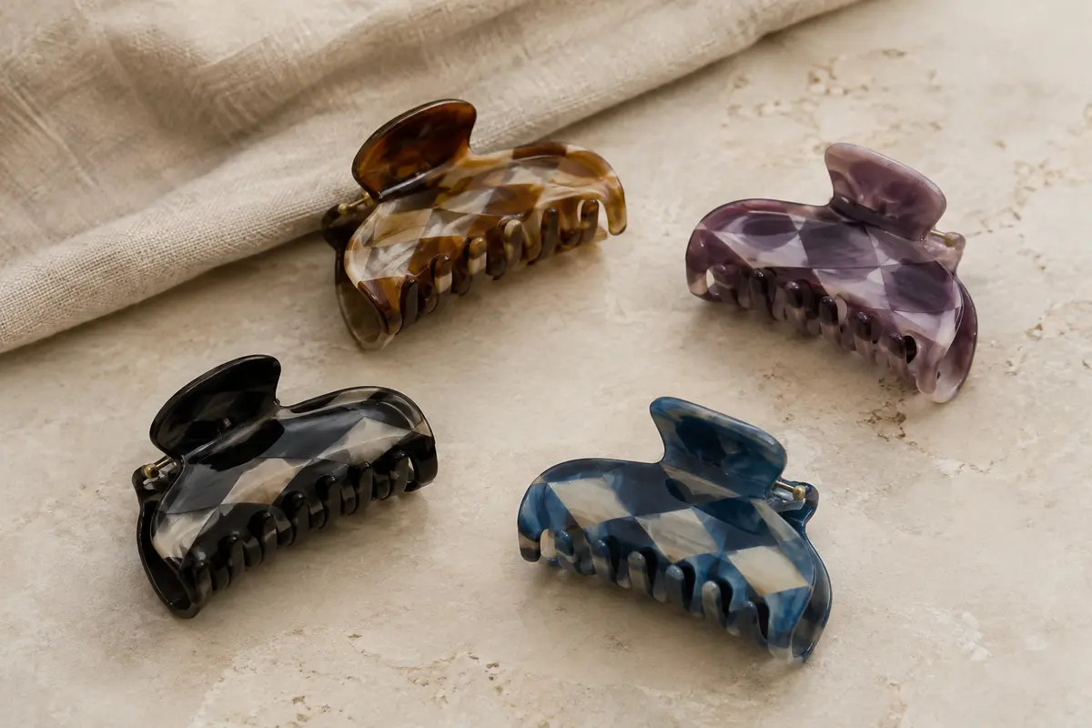 Quatre pinces à cheveux en acrylique aux teintes variées, posées sur une surface claire avec du lin