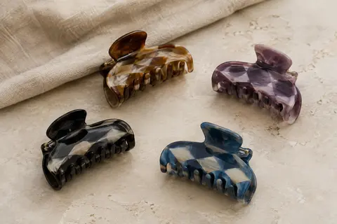 Quatre pinces à cheveux en acrylique aux teintes variées, posées sur une surface claire avec du lin