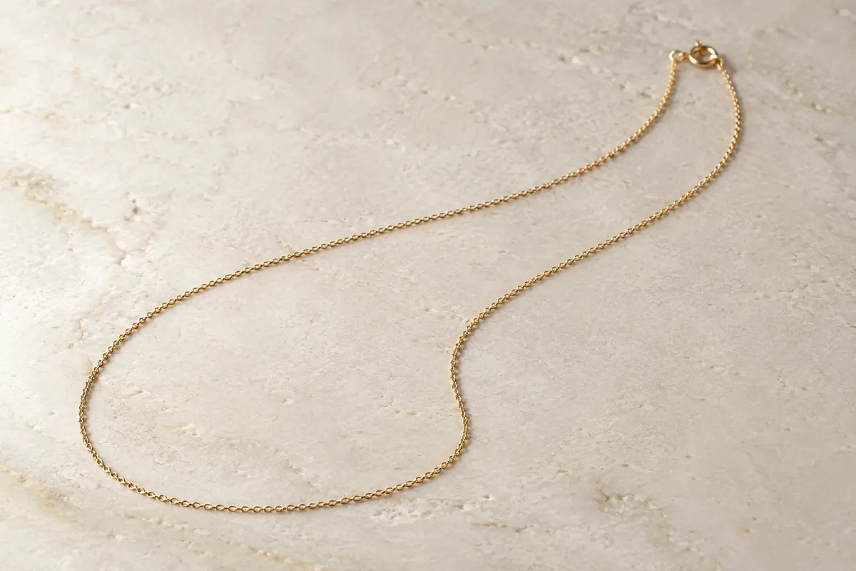 Chaîne fine de 1 mm en argent sterling plaqué or, posée seule sur une surface minérale claire.