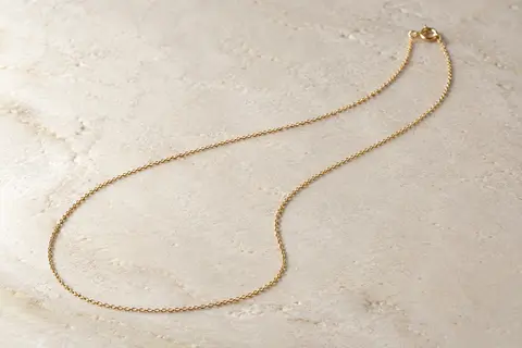 Chaîne fine de 1 mm en argent sterling plaqué or, posée seule sur une surface minérale claire.