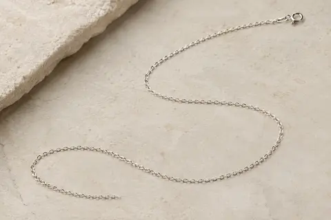 Chaîne longue fine en argent 925, disposée en courbe sur une surface minérale claire