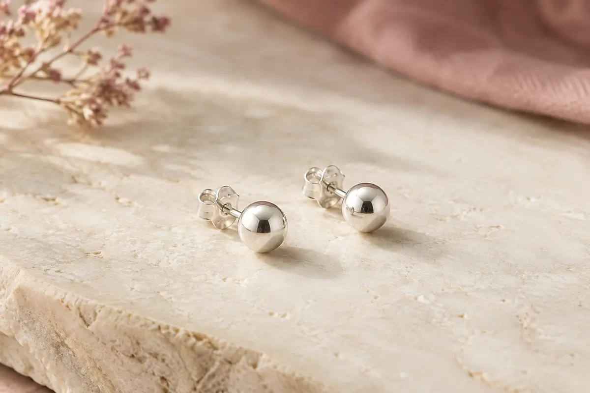 Paire de puces d’oreilles boule en argent 925 posée sur une surface minérale claire.