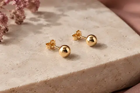 Puces d’oreilles rondes dorées à tige présentées seules sur une surface minérale claire.