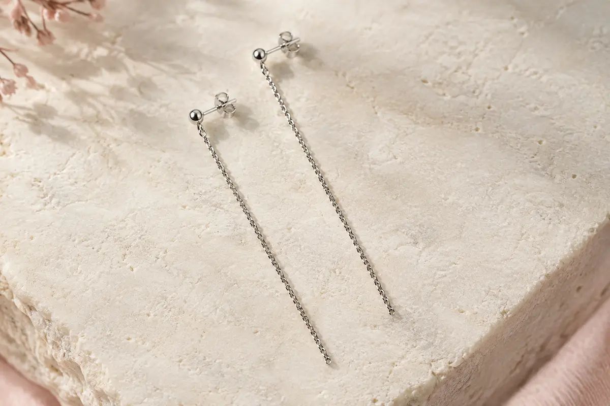 Paire de boucles pendantes à pampilles longues en argent, posée sur une surface minérale claire.