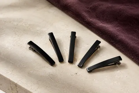 Lot de barrettes à cheveux noires en métal, disposées sur une surface claire avec un fond prune