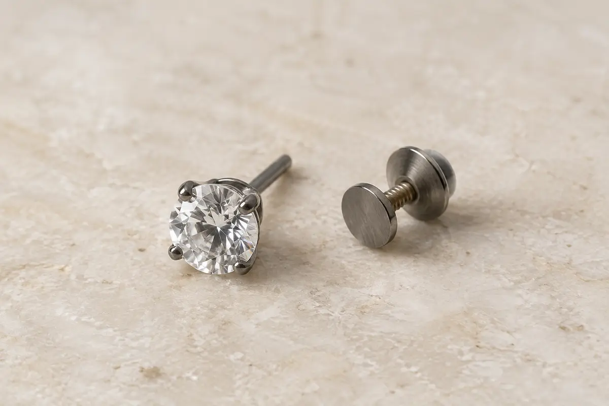 Puce d’oreille en titane gris avec zircone cubique et fermoir vissé, posée sur une surface minérale claire.