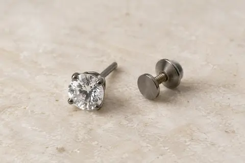 Puce d’oreille en titane gris avec zircone cubique et fermoir vissé, posée sur une surface minérale claire.