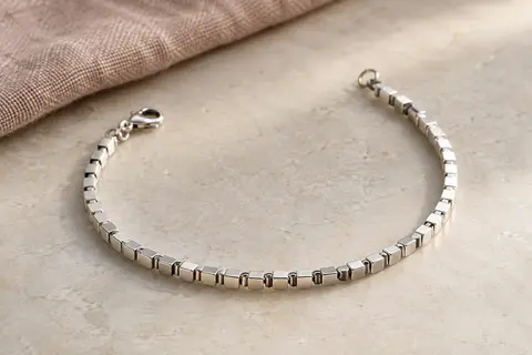 Bracelet en argent 925 à chaîne de cubes et fermoir mousqueton, posé sur une surface minérale claire.