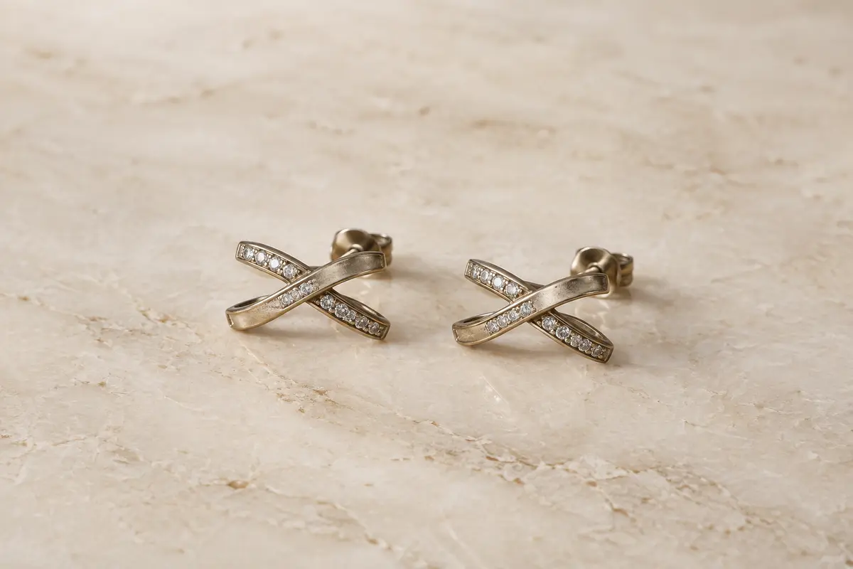 Paire de puces d’oreilles au motif croisé et zircones cubiques, présentée seule sur une surface claire.