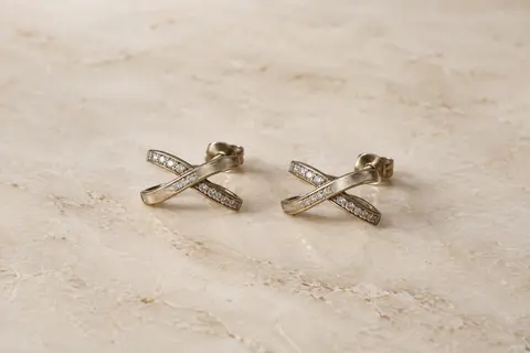 Paire de puces d’oreilles au motif croisé et zircones cubiques, présentée seule sur une surface claire.