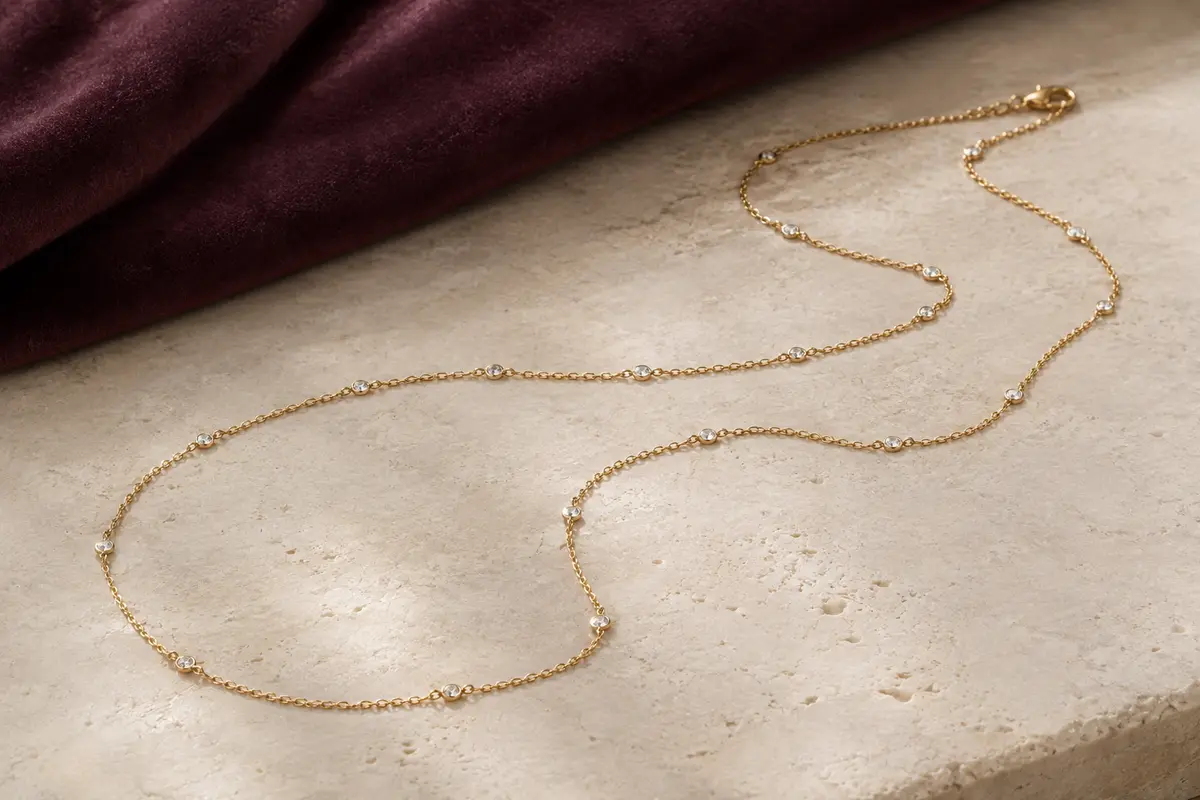 Sautoir doré en laiton plaqué or, ponctué de zircons et disposé sur une surface claire avec du velours prune.
