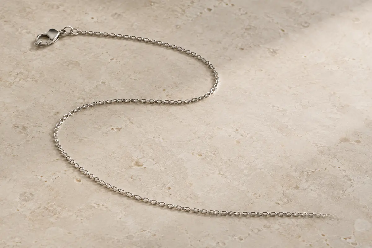 Chaîne gourmette fine en argent rhodié disposée seule sur une surface minérale claire
