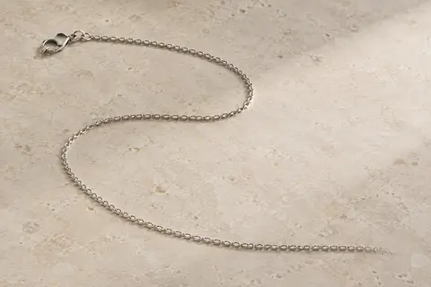 Chaîne gourmette fine en argent rhodié disposée seule sur une surface minérale claire
