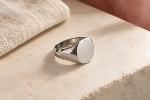 Chevalière argentée en acier inoxydable à dessus plat, présentée seule sur une surface minérale claire.