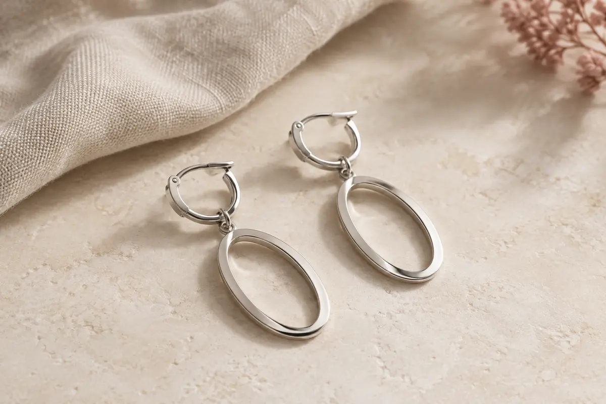 Paire de boucles d’oreilles ovales argentées à arceau articulé posées sur une surface claire
