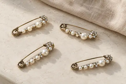 Quatre broches en forme d’épingle, ornées de perles imitation et de cristaux, sur une surface claire.