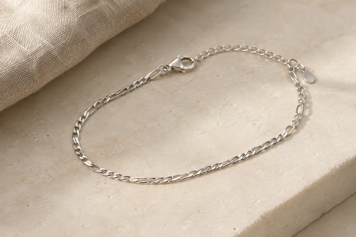 Bracelet de cheville en argent 925 à maille Figaro, avec extension et fermoir mousqueton, posé sur du lin clair.
