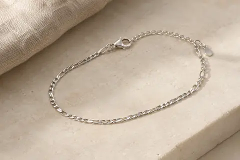 Bracelet de cheville en argent 925 à maille Figaro, avec extension et fermoir mousqueton, posé sur du lin clair.