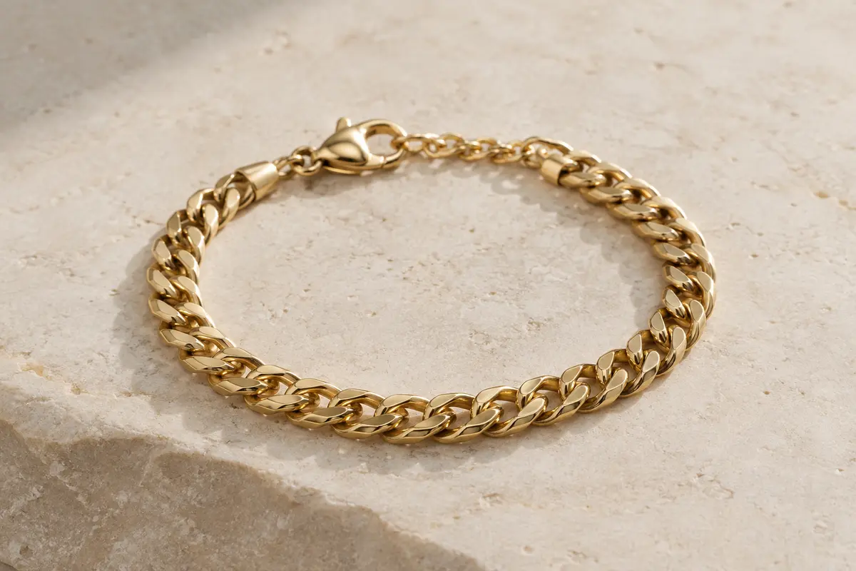 Bracelet gourmette doré à maille cubaine posé sur une surface minérale claire, éclairé doucement.
