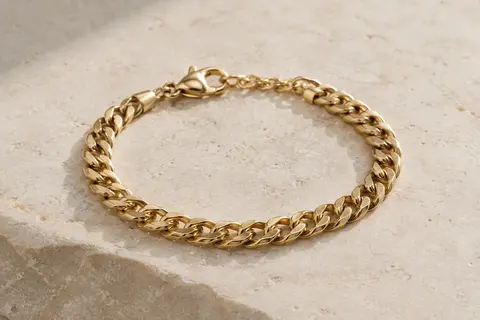 Bracelet gourmette doré à maille cubaine posé sur une surface minérale claire, éclairé doucement.