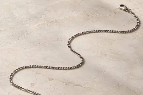 Chaîne cubaine fine en acier inoxydable posée en courbe sur une surface minérale ivoire