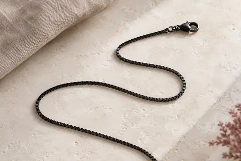 Chaîne PROSTEEL noire à maille boîte aplatie, posée en courbe sur une surface minérale claire