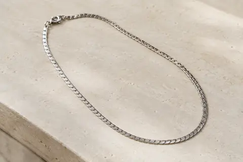 Chaîne ras du cou PROSTEEL à maille miroir plate, disposée seule sur une surface minérale claire.